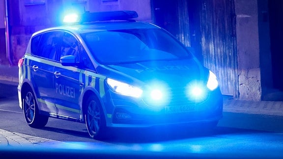 Ein Fahrzeug der Polizei fährt mit Blaulicht am Abend durch eine enge Straße.