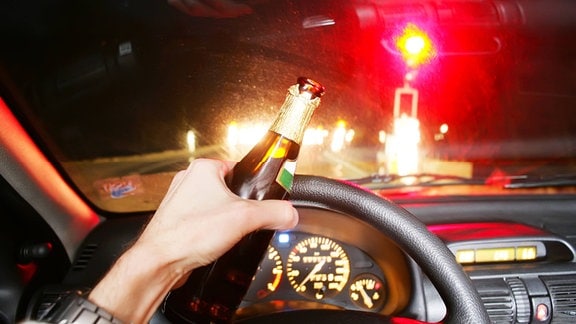 Ein Autofahrer hält eine Bierflasche in der Hand.