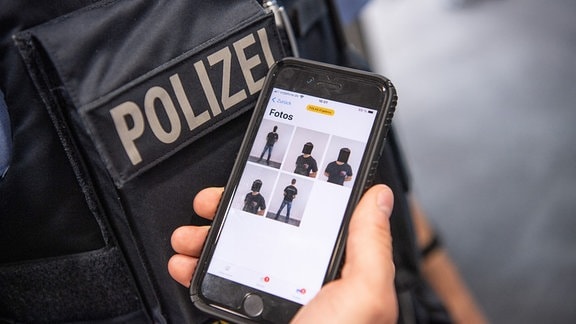 Ein Polizist zeigt zu Demonstrationszwecken auf seinem Smartphone eine spezielle Polizei-App mit den Fotos eines fiktiven Verdächtigen.