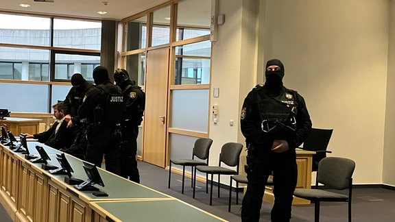 Vier bewaffnete Polizisten bewachen den Halle-Attentäter, der neben seinem Anwalt im Gerichtssaal sitzt.
