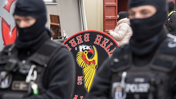 Polizeibeamte stehen vor dem Gelände der Rockergruppe "Hells Angels MC Berlin Central" in Berlin. Im Hintergrund ist das Logo der Gruppe zu sehen.