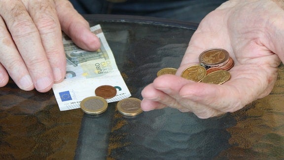 Ein Rentner hält eine Geldbörse und Geld in den Händen.