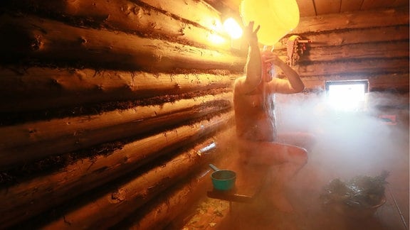 Ein Mann in einer Sauna kippt sich Wasser über den Kopf.