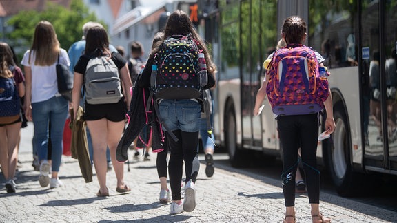 Schülerinnen gehen 2019 an einer Bushaltestelle zu stehenden Bussen.