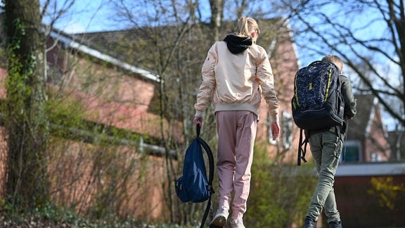 Eine Schülerin geht in einer Jogginghose auf dem Schulhof einer Schule.