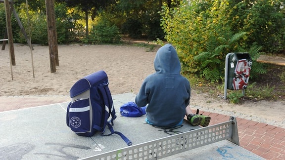 Ein Junge sitzt mit seinem Schulranzen auf einer Tischtennisplatte auf einem Spielplatz
