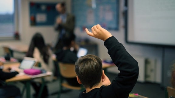 Eine Schüler hebt im digitalen Unterricht seine Hand hoch.