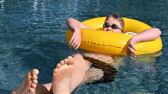 Ein Kind in einem gelben Schwimmreifen in einem Freibad.