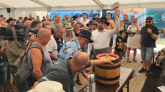 Menschen bei einem Bierfassanstich in einem Festzelt.