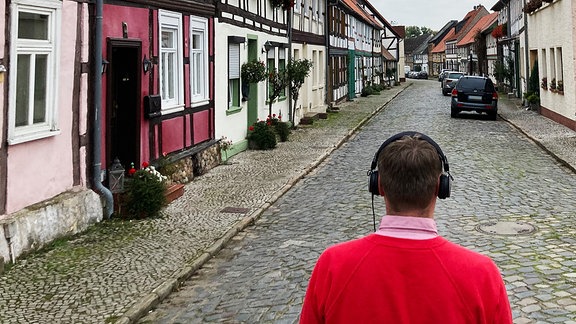 Mann mit Kopfhörern auf einer Straße mit Fachwerkhäusern
