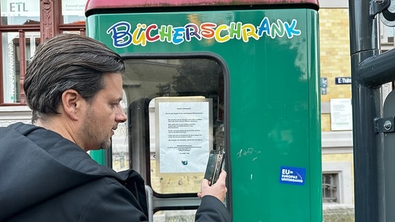 Ein Mann fotografiert einen Sticker auf einer Telefonzelle