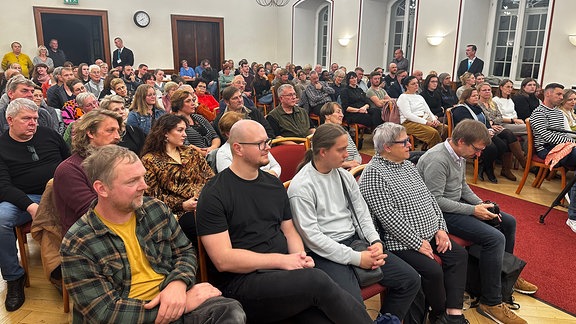 Mehrere Menschen sitzen auf Stühlen in einem Saal