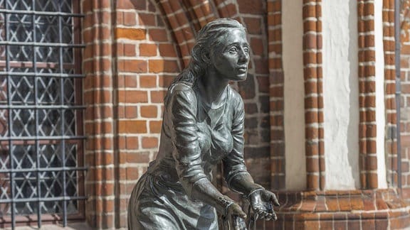 Eine Skulptur von einer Frau vor einem alten Backsteingebäude.  
