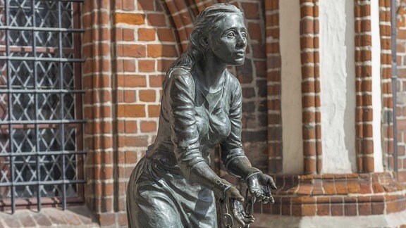 Eine Skulptur von einer Frau vor einem alten Backsteingebäude.  