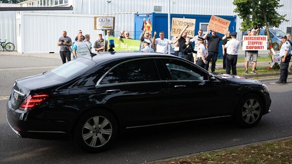 Das Auto von Robert Habeck (Bündnis 90/Die Grünen), Bundesminister für Wirtschaft und Klimaschutz, fährt vor einem Besuch des Bauunternehmens Ost Bau im Rahmen der Sommerreise des Bundeswirtschaftsminister an Demonstranten vorbei.