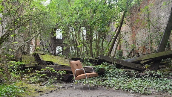 Im verlassenen zugewucherten Innenhof eines alten Backsteingebäudes steht ein zerschlissener Stuhl