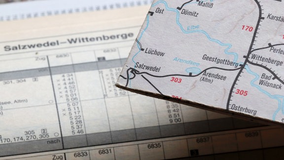Auf einer Karte ist die Bahnstrecke Salzwedel-Arendsee verzeichnet, im Hintergrund ist eine Fahrplantabelle zu sehen