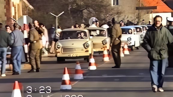 Eine lange Reihe Trabis an einem Grenzübergang, dazwischen sind Grenzer und Passanten zu sehen