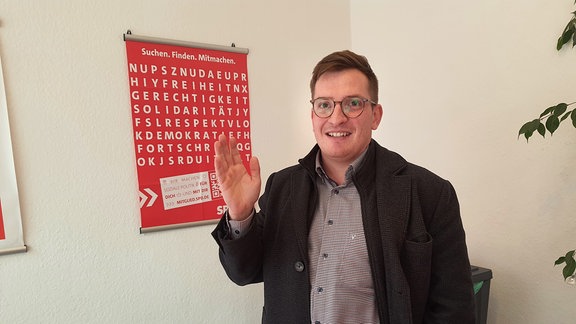 Ein Mann steht in einem Raum vor einer Wand mit SPD-Plakat. 