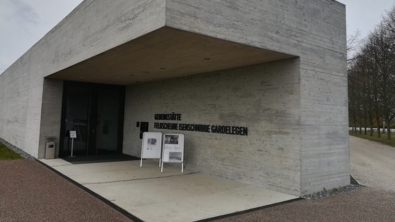 Ein flaches Gebäude aus Beton mit dem Schriftzug "Gedenkstätte Feldscheune Isenschnibbe Gardelegen"