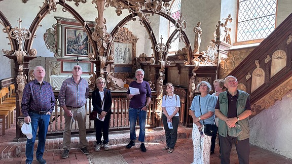 Eine Gruppe aus acht Personen steht in einer Kirche und bestaunt die Holzschnitzereien im Inneren