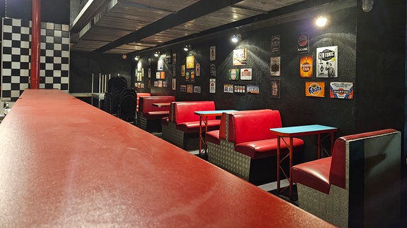 Blick in eine Bar. Tische und Stühle sind rot bezogen und im Retro-Look gestaltet. 