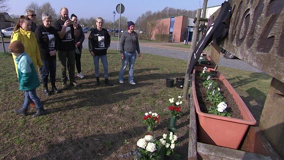 Mehrere Menschen vor einer Parkbank des VfB Klötze mit Blumen und Kerzen in Gedenken an die getötete Khezia