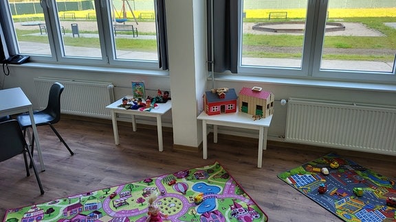 Kinderspielzimmer mit Spielzeug und Sitzgruppen - durch das Fenster ist der Kinderspielplatz zu sehen. 