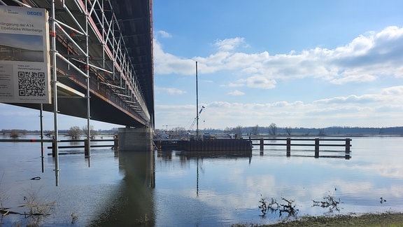 Blick auf eine Brücke über einem Fluss, der leicht über die Ufer getreten ist.