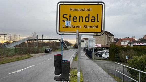 Am Ortsschild der Hansestadt Stendal hängt ein paar Gummistiefel. 