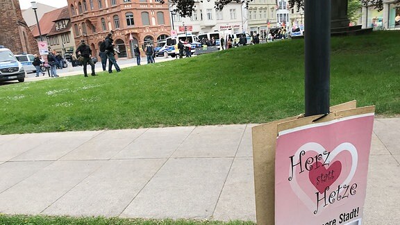 Plakat Herz statt Hetze, im Hintergrund eine Demo und Polizei.