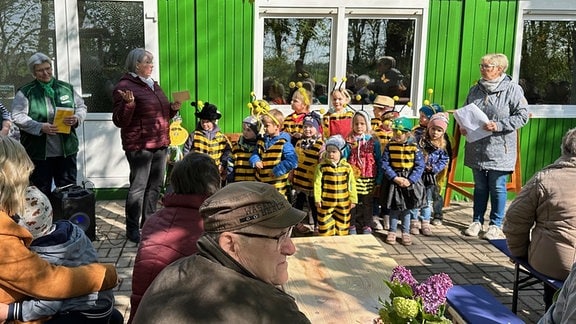 Vor einem grünen Gebäude steht eine Gruppe Kinder im Bienenkostm