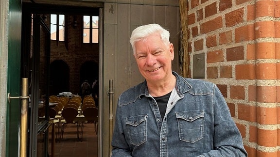 Ein Mann steht vor einer Kirche und lächelt in die Kamera