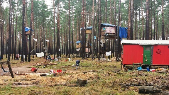 Baumhäuser und ein roter alter Campingwagen in einem Waldstück