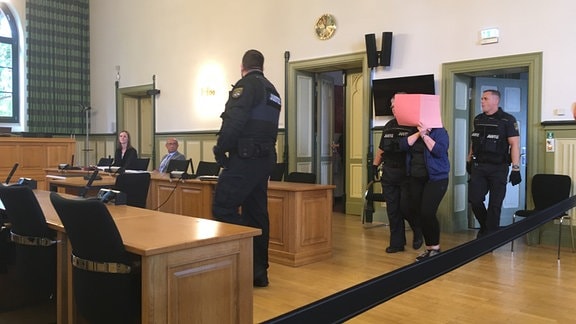 Mitarbeitende der Justiz und Frau, die sich das Gesicht verdeckt, in Gerichtssaal Eingang des Landgerichts Stendal