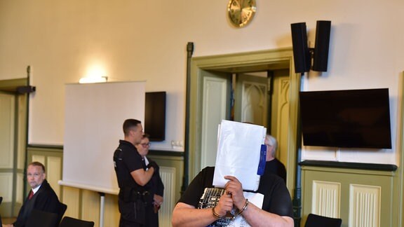 Ein Angeklagter verdeckt sein Gesicht beim Betreten des Saals im Landgericht Stendal vor der Urteilsverkündung um Angriffe auf Klima-Aktivisten in Seehausen vom 18. Juni 2021. 