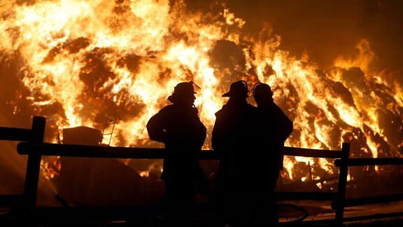 Feuerwehrleute stehen vor brennenden Strohballen.