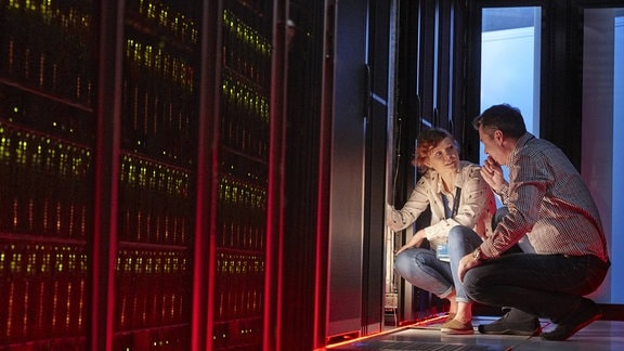 IT-Techniker unterhalten sich an leuchtendem Panel im dunklen Serverraum