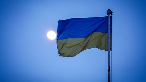Die Flagge der Ukraine weht über der Hafenstadt im Mondlicht im Wind.