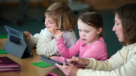 Schülerinnen der Klassenstufe 1-3 der Berliner Hunsrück-Grundschule lösen im Mathematik-Unterricht mit Hilfe ihrer Lehrerin am Tablet eine Rechenaufgabe.