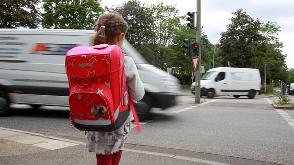Ein Mädchen steht auf dem Schulkweg an einer roten Fußgängerampel.
