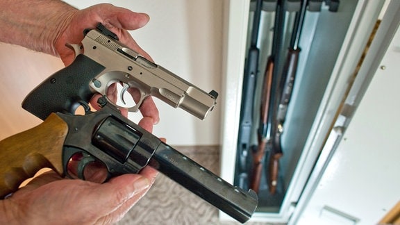 Ein Sportschütze zeigt 2009 eine Pistole und einen Revolver vor einem Waffenschrank mit drei Gewehren in einem privaten Haushalt.