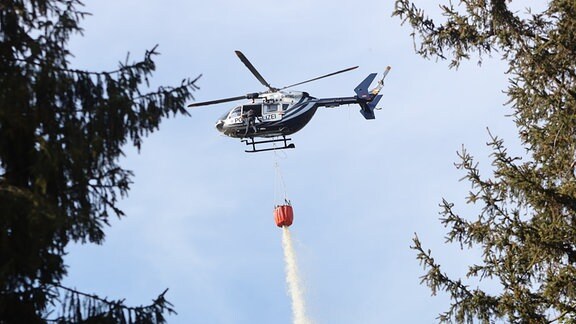 Ein Polizeihubschrauber bringt Wasser zum Löschen an einen Waldbrand bei Stiege im Harz
