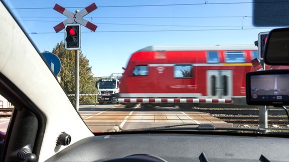 Blick aus einem Pkw an einem beschrankten Bahnübergang, den ein Regionalzug passiert