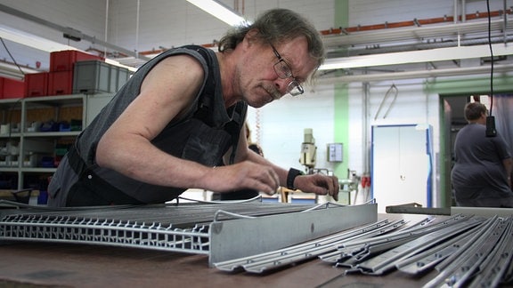 Menschen arbeiten in einer Werkstatt. Ein Mann ordnet Metallstreifen.