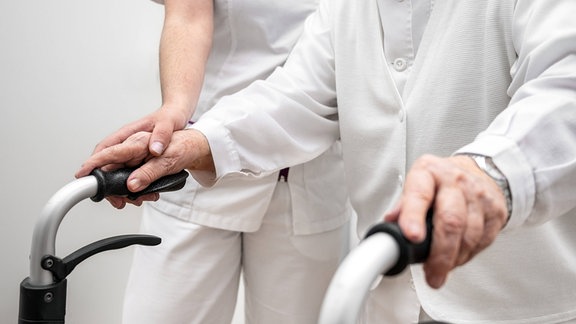 Krankenschwester hilft ihrer älteren Patientin mit einer klappbaren Gehhilfe.
