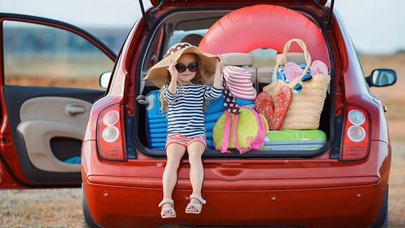 Ein Mädchen sitzt im voll beladenen Kofferraum eines Kleinwagens