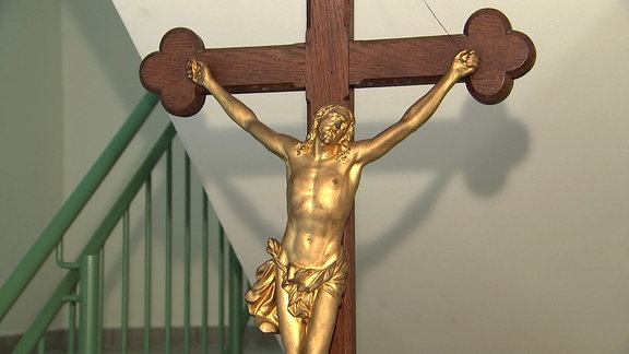 Ein goldener Jesus an einem Holzkreuz.