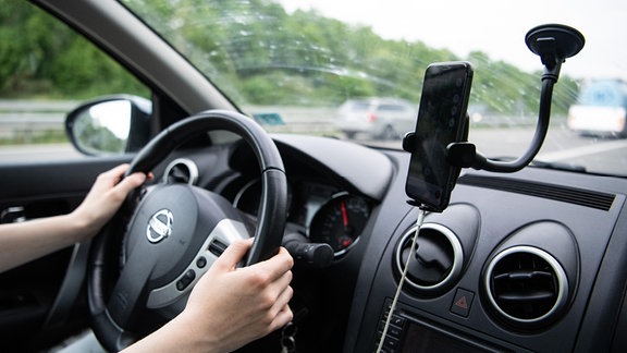Eine Frau sitzt im Auto mit Handy in einer Halterung.