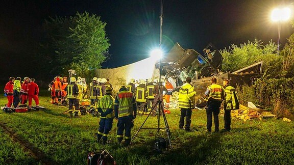 Feuerwehrleute, Polizisten und Rettungskräfte auf einer Wiese vor einem umgekippten, schwer beschädigten Lkw.